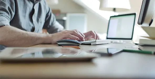 A person using a laptop on top of a wooden table.